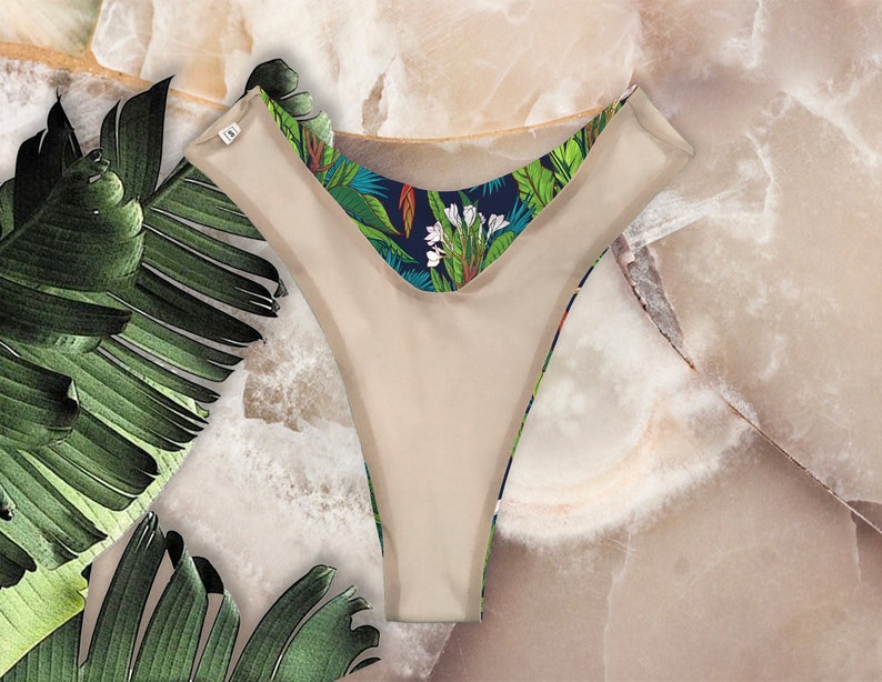 May include: Beige underwear with a tropical print on the waistband. The print features green leaves, white flowers, and blue accents.