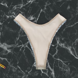 May include: Black and white patterned bikini bottom with a nude lining. The bikini bottom is made of a soft, stretchy fabric.