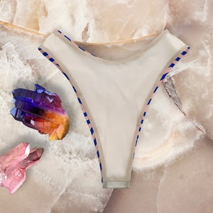 May include: White bikini bottom with blue and pink striped trim. The bikini bottom is lying on a white marble surface with colorful crystals.