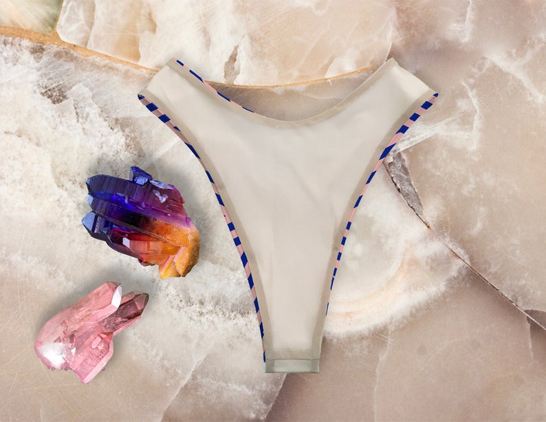 May include: White bikini bottom with blue and pink striped trim. The bikini bottom is lying on a white marble surface with colorful crystals.