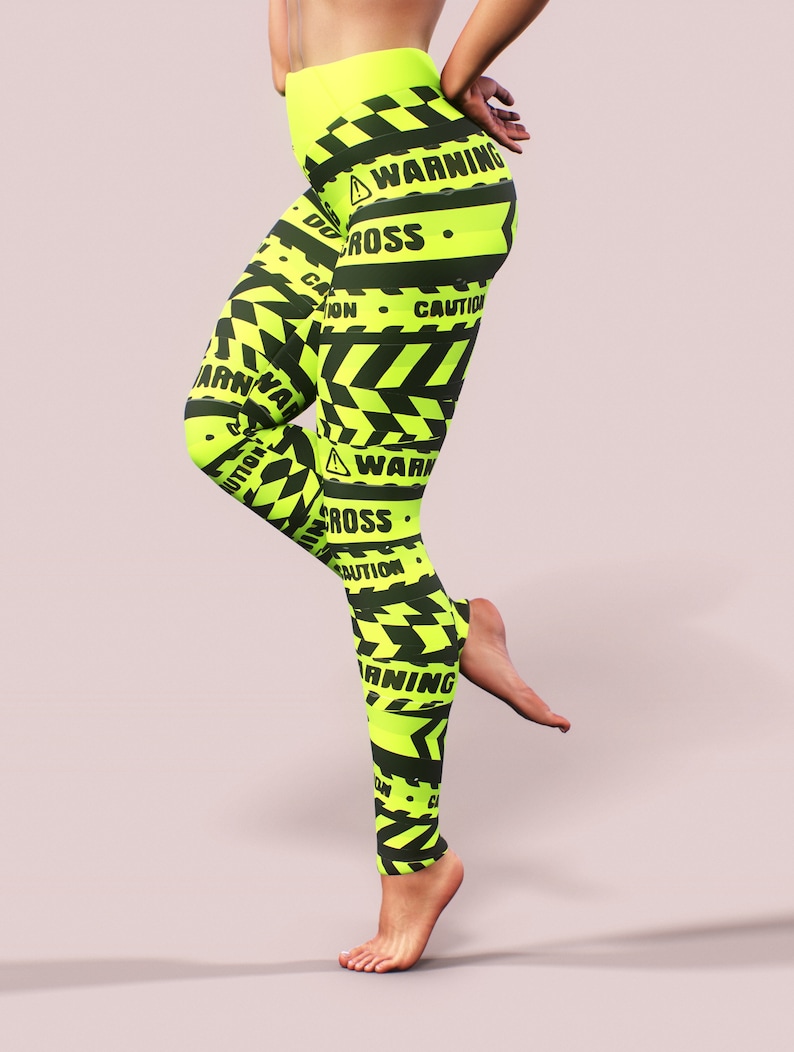 May include: Neon yellow leggings with black warning tape design. The leggings feature the words "WARNING", "CAUTION", and "DO NOT CROSS" in black. The leggings have a high waist and a form-fitting design.