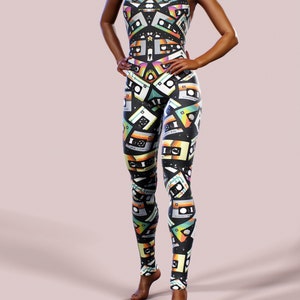 May include: A black jumpsuit with a colourful cassette tape pattern. The jumpsuit has a high neckline and sleeveless design.