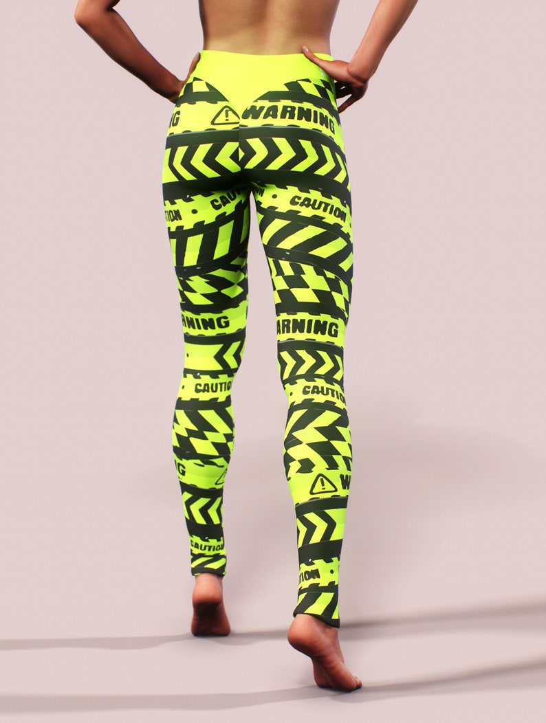 May include: Neon yellow leggings with a black caution tape design. The leggings feature the words "WARNING" and "CAUTION" in black, along with hazard symbols. The leggings are form-fitting and high-waisted.