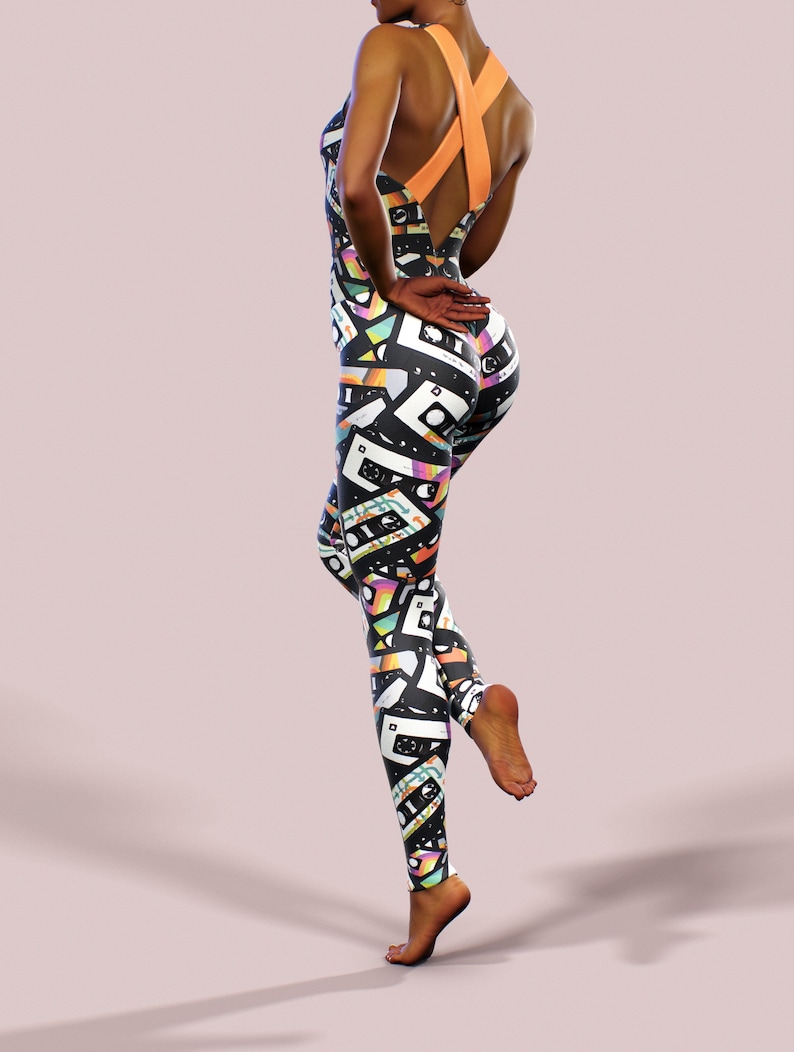 May include: Black and white jumpsuit with a colourful cassette tape pattern. The jumpsuit has a criss-cross back strap and a scoop neck.