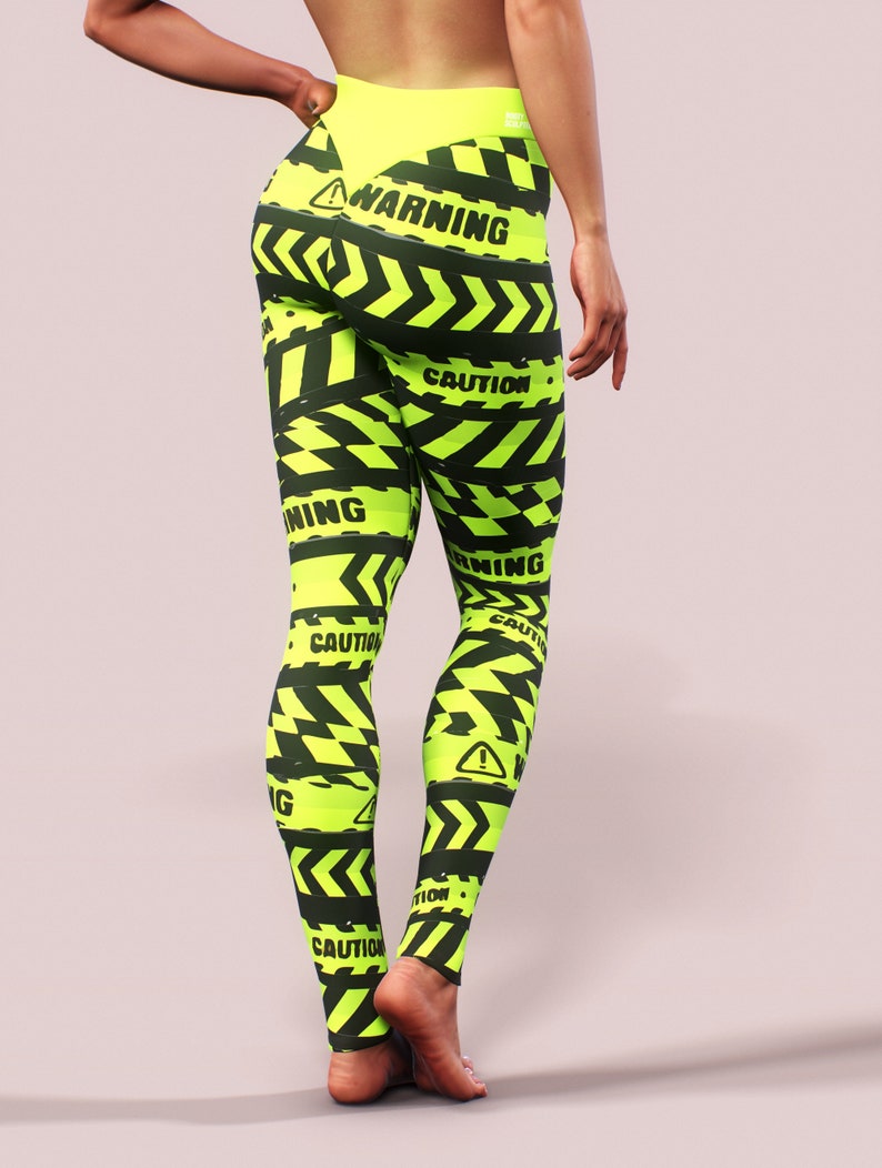 May include: Neon green leggings with a black hazard stripe pattern and the words "WARNING" and "CAUTION" printed throughout. The leggings have a high waist and a matching neon green waistband.