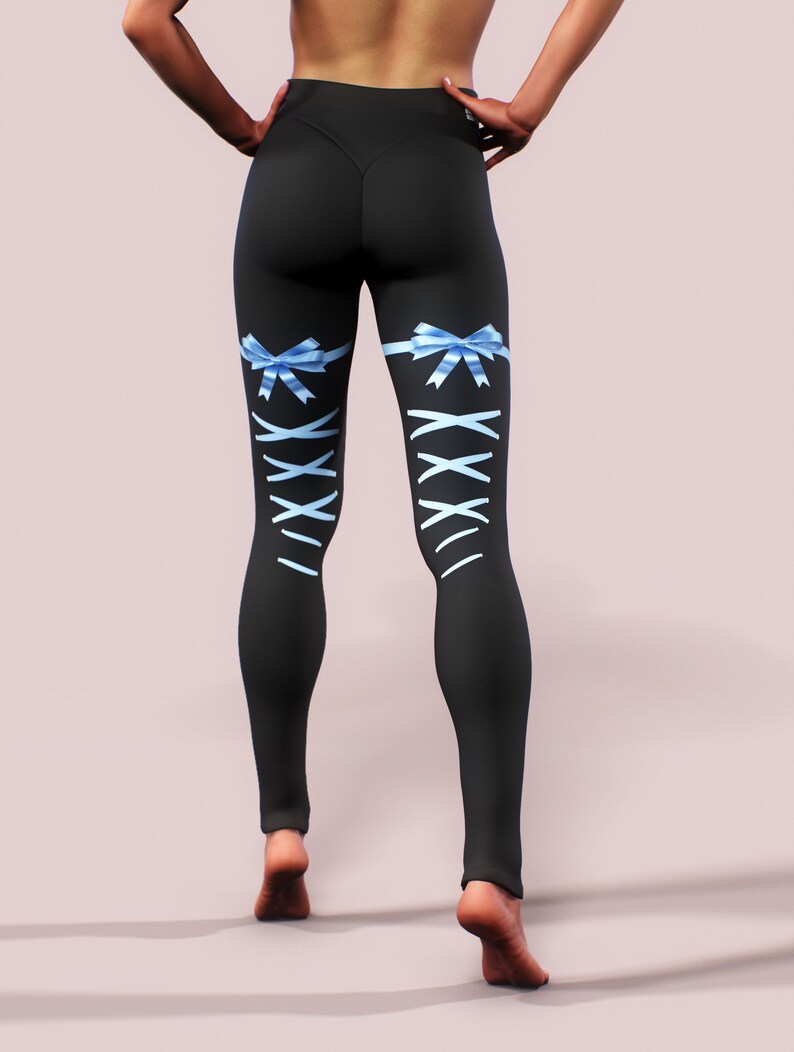 Pu&ograve; includere: Leggings neri con fiocchi di nastro azzurro chiaro e design a stringhe bianche incrociate sulla parte inferiore delle gambe. I leggings sono a vita alta e aderenti. La modella &egrave; in piedi con le mani sui fianchi.