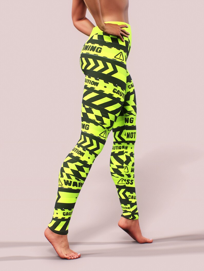 May include: Neon yellow leggings with a black caution tape design. The leggings feature the words "WARNING" and "CAUTION" in black, along with hazard symbols. The leggings are form-fitting and made of a stretchy material.