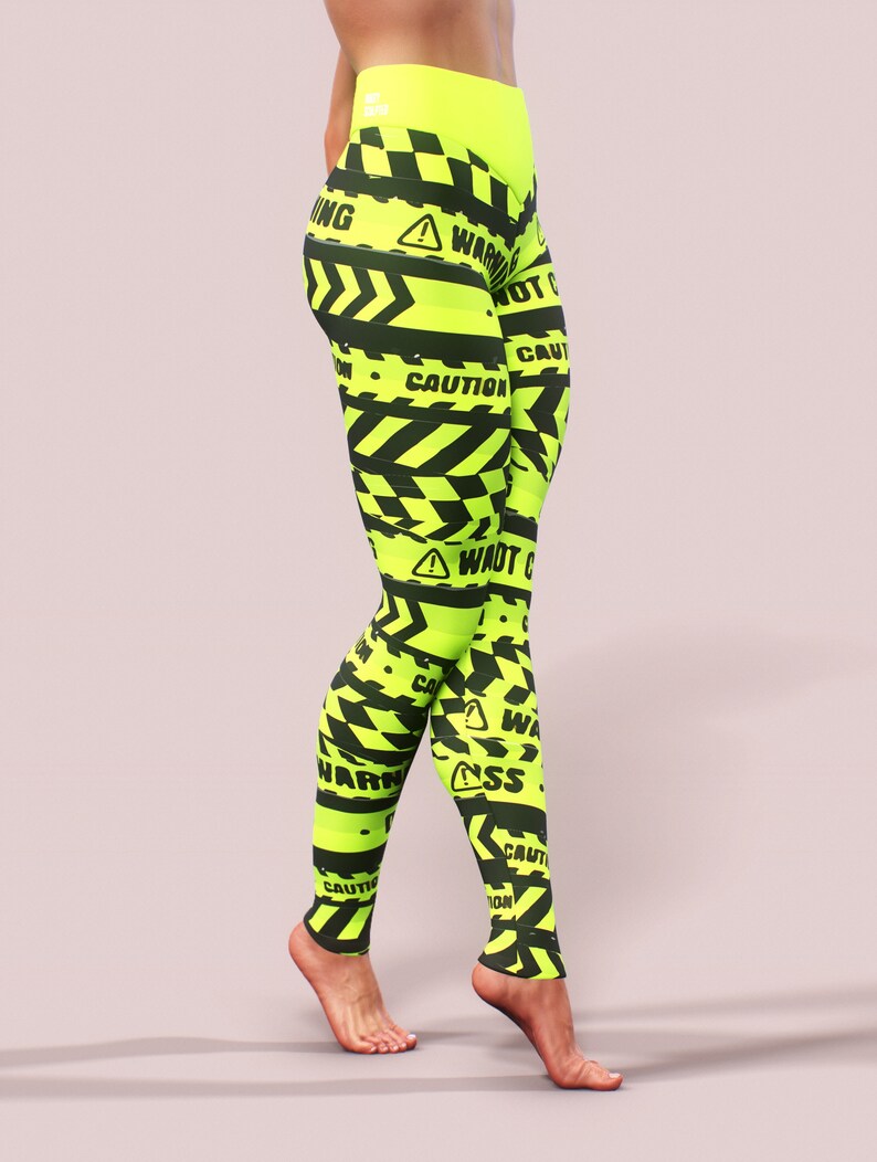May include: Neon yellow leggings with a black warning tape design. The leggings feature the words "WARNING" and "CAUTION" in black, along with hazard symbols. The high-waisted leggings are made of a stretchy material.