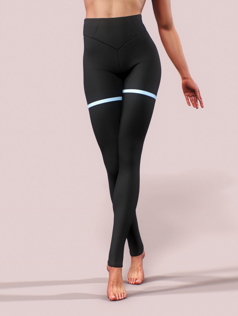 Pu&ograve; includere: Leggings neri con vita alta e un dettaglio a striscia orizzontale azzurra sulla parte superiore della coscia. I leggings sono aderenti e realizzati in un materiale liscio. La modella &egrave; in piedi su uno sfondo rosa chiaro.