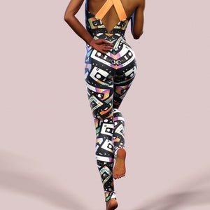 May include: Black and white jumpsuit with a colourful cassette tape pattern. The jumpsuit has a criss-cross strap design at the back.