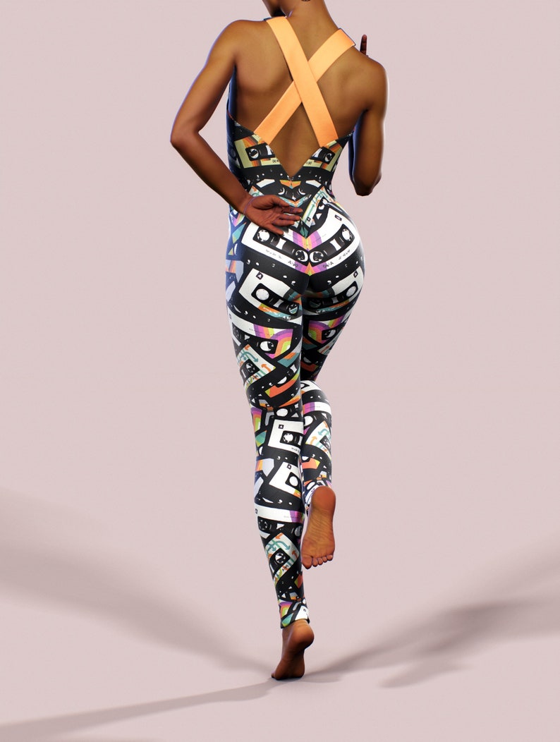 May include: Black and white jumpsuit with a colourful cassette tape pattern. The jumpsuit has a criss-cross strap design at the back.