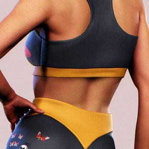 May include: A black and yellow sports bra with a racerback design. The bra has a yellow band at the bottom. The model is wearing matching black and yellow leggings with a butterfly print.