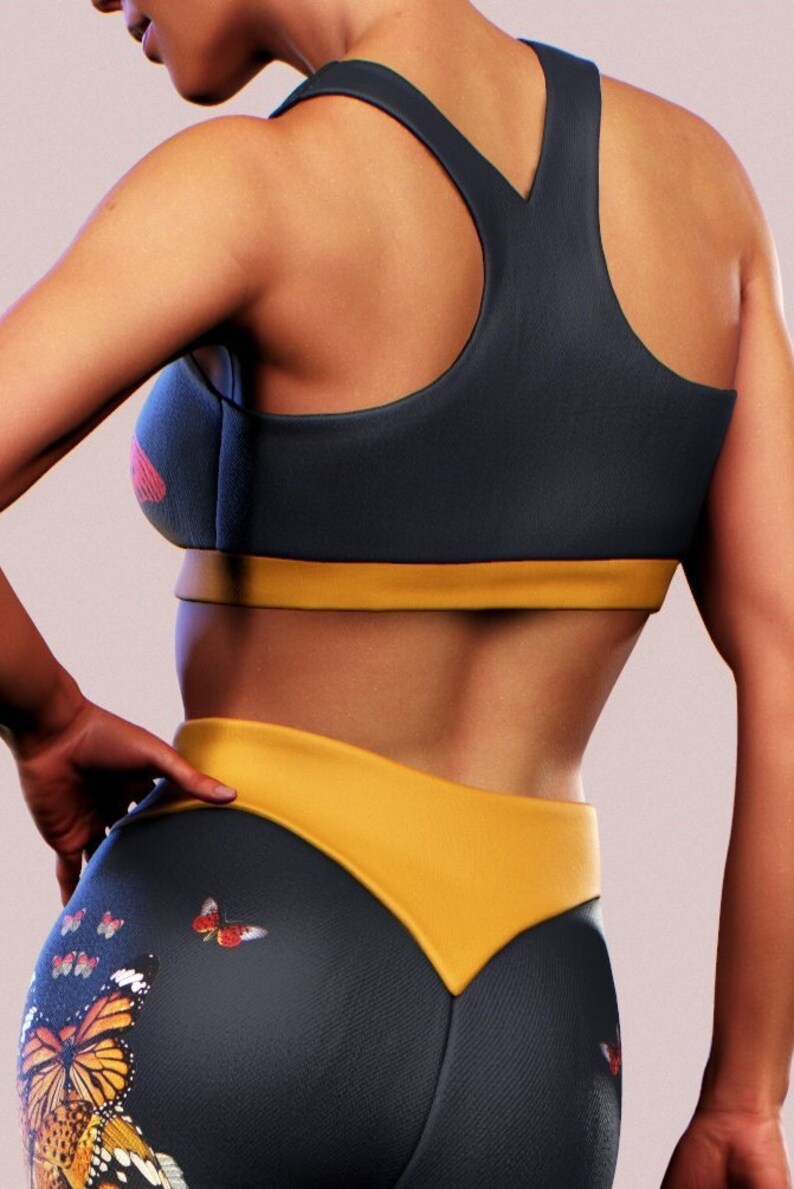 May include: A black and yellow sports bra with a racerback design. The bra has a yellow band at the bottom. The model is wearing matching black and yellow leggings with a butterfly print.