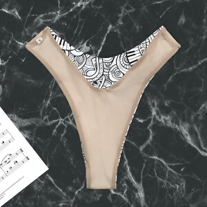 May include: A black and white patterned thong with a nude lining. The pattern features musical notes and piano keys.