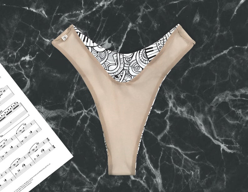 May include: A black and white patterned thong with a nude lining. The pattern features musical notes and piano keys.