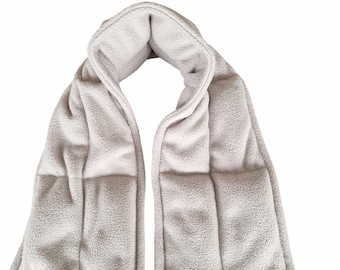 May include: A light grey, plush neck wrap with a quilted design. The wrap is made of a soft, textured material and is designed to be worn around the neck. It has a tag attached at the bottom.