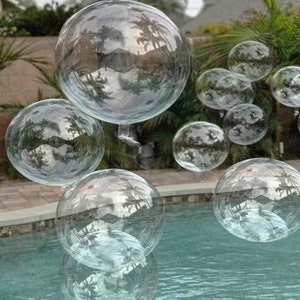May include: A group of clear plastic balloons floating in a swimming pool. The balloons are large and round, and they reflect the surrounding environment.