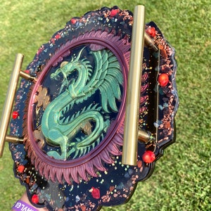 May include: A black resin tray with a gold metal handle. The tray features a green dragon design with red and gold accents. The tray is decorated with glitter and small red and gold pieces.