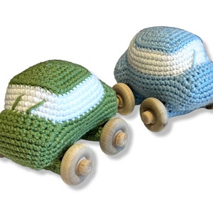 May include: Two crocheted toy cars. One is green with a white stripe across the top, and the other is light blue with a white stripe. Both have wooden wheels.