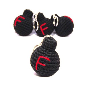 May include: Black crocheted keychains with a red "F" design. The keychains are handmade and have a round shape with a small loop for the key ring. The keychains are displayed on a white background.