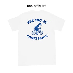 May include: White t-shirt with a blue graphic of a person riding a bicycle, and the text "SEE YOU AT CONFESSION" in blue. The back of the shirt is visible.