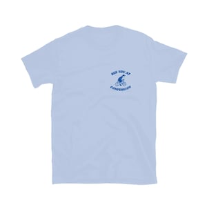 May include: Light blue t-shirt with a small blue graphic of a person riding a bicycle and the text "SEE YOU AT CONFESSION". The shirt has short sleeves and a crew neck.