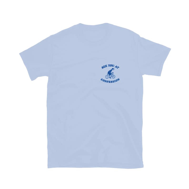 May include: Light blue t-shirt with a small blue graphic of a person riding a bicycle and the text "SEE YOU AT CONFESSION". The shirt has short sleeves and a crew neck.