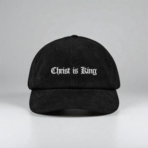 Könnte beinhalten: Schwarze Cord-Baseballkappe mit dem weißen Schriftzug "Christ is King". Die Kappe hat einen gebogenen Schirm und einen verstellbaren Riemen auf der Rückseite. Ein klassischer Hut für den Alltag.