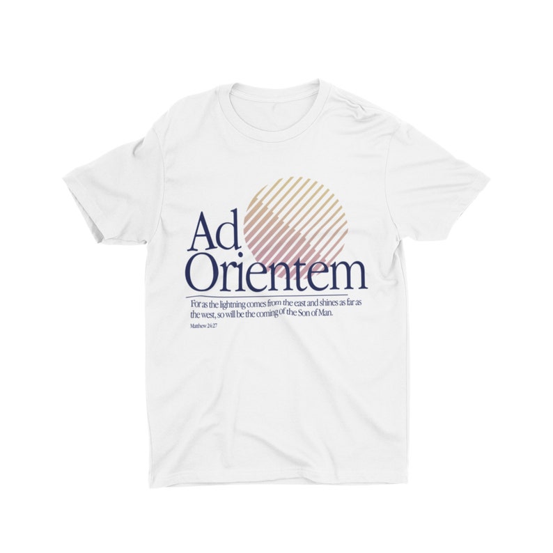 May include: White t-shirt with a graphic of a sun with a striped pattern in pink and brown. The text "Ad Orientem" is printed in navy blue below the sun. The text "For as the lightning comes from the east and shines as far as the west, so will be the coming of the Son of Man. Matthew 24:27" is printed in navy blue below the graphic.