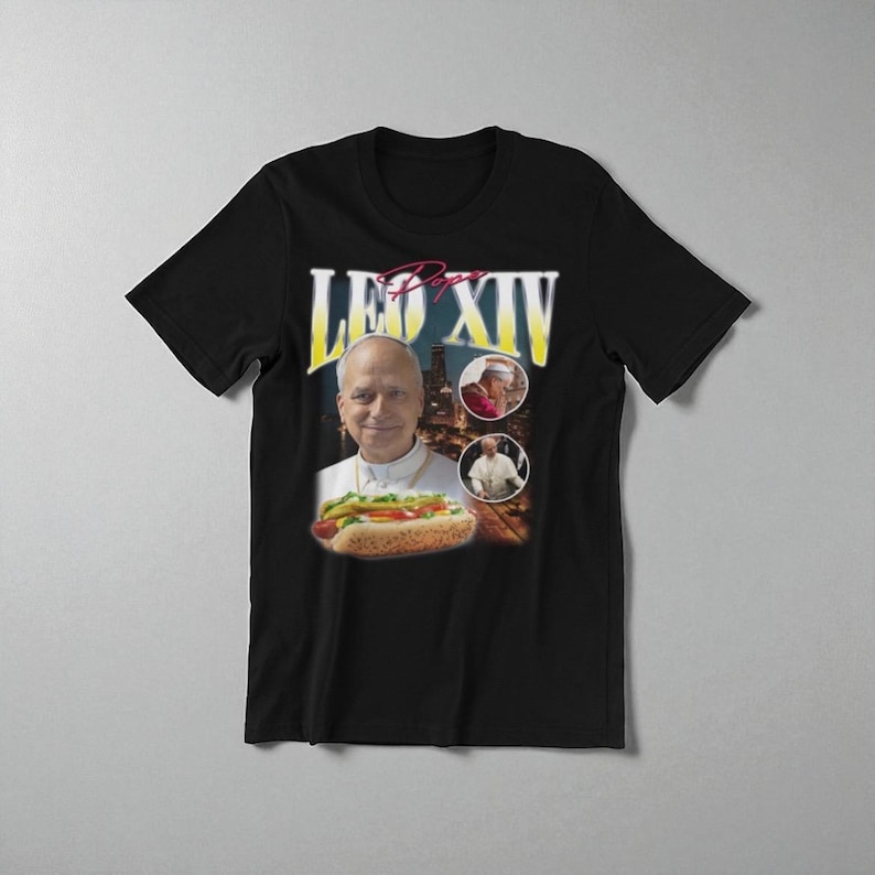 K&ouml;nnte beinhalten: Schwarzes T-Shirt mit einer Grafik eines Mannes, der einen Hotdog h&auml;lt, mit dem Text "Leo XIV" in Gelb und Rot. Zwei kleinere Bilder sind ebenfalls enthalten. Das T-Shirt hat einen klassischen Rundhalsausschnitt.