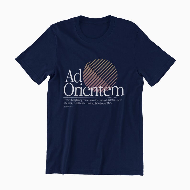 May include: Navy blue t-shirt with a white graphic of a sun with stripes and the text "Ad Orientem". The text below the graphic reads "For as the lightning comes from the east and shines as far as the west, so will be the coming of the Son of Man".