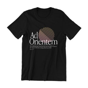 May include: Black t-shirt with a graphic of a sun with a pink and orange gradient and the text "Ad Orientem". The text below the graphic reads "For as the lightning comes from the east and shines as far as the west, so will be the coming of the Son of Man. Matthew 24:27"