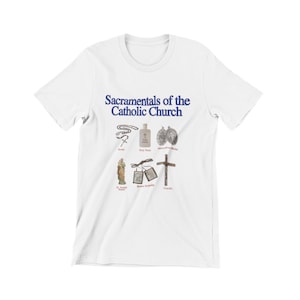 Puede incluir: Camiseta blanca con texto azul que dice "Sacramentals of the Catholic Church". La camiseta presenta una ilustración de varios sacramentales católicos, incluyendo un rosario, agua bendita, una medalla milagrosa, una estatua de San José, un escapulario marrón y un crucifijo.