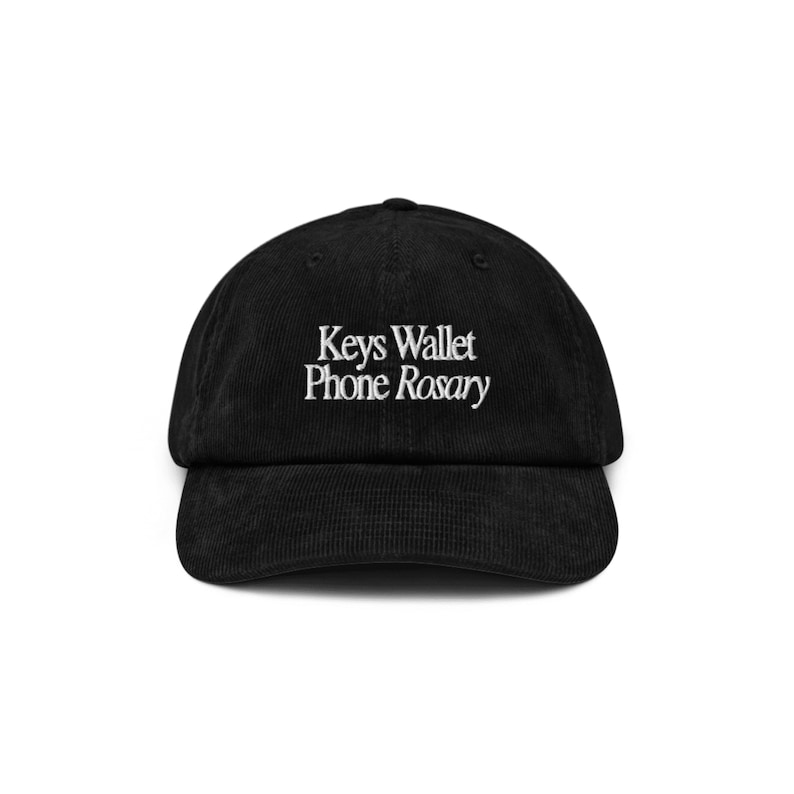 May include: A black corduroy baseball cap with white embroidered text that reads "Keys Wallet Phone Rosary".