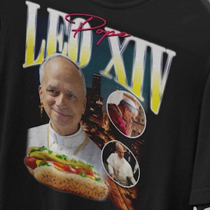 K&ouml;nnte beinhalten: Schwarzes T-Shirt mit einer humorvollen Grafik einer als Papst verkleideten Person, die einen Hotdog h&auml;lt. Das Design enth&auml;lt den Text "LEO XIV" in gelber und wei&szlig;er Schrift, mit dem Wort "Pope" in Rosa.