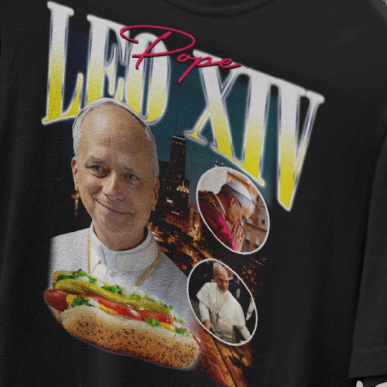 K&ouml;nnte beinhalten: Schwarzes T-Shirt mit einer humorvollen Grafik einer als Papst verkleideten Person, die einen Hotdog h&auml;lt. Das Design enth&auml;lt den Text "LEO XIV" in gelber und wei&szlig;er Schrift, mit dem Wort "Pope" in Rosa.