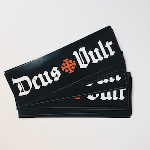 May include: A stack of black stickers with the text "Deus Vult" in white lettering and a red cross in the middle.