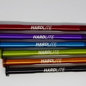 May include: Six different colored bicycle thru axles with the text "HARDLITE" printed on each. The axles are made of aluminum and are available in red, purple, blue, green, orange, and black.