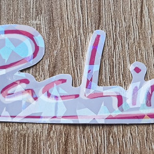 K&ouml;nnte beinhalten: Ein holografischer Aufkleber mit dem Wort "Palio" in pinker Kursivschrift.