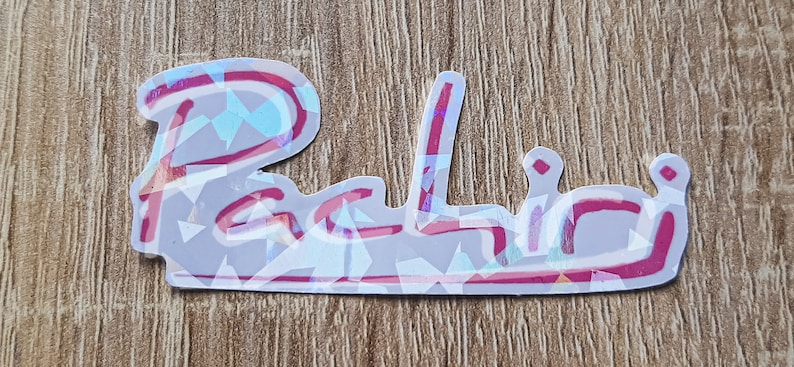 K&ouml;nnte beinhalten: Ein holografischer Aufkleber mit dem Wort "Palio" in pinker Kursivschrift.