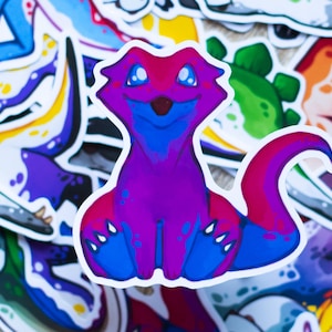 Könnte beinhalten: Ein Aufkleber mit einer Cartoon-Kreatur in rosa, blau und lila. Die Kreatur hat einen langen Schwanz und sitzt auf ihren Hinterbeinen. Der Aufkleber ist auf weißem Hintergrund.