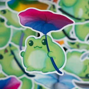May include: A green frog sticker with a pink, blue, and purple umbrella. The frog is holding the umbrella with its right hand. The sticker is on a white background.