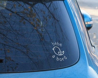 Puede incluir: Un coche azul con una pegatina blanca en la ventana trasera que dice "bebe a bord" con una pequeña ilustración de un pájaro.