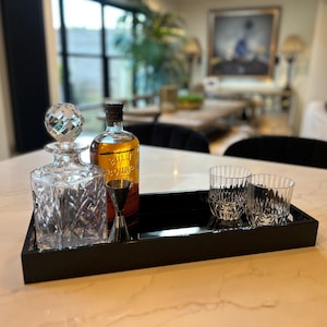 May include: A black tray with a clear glass decanter, a bottle of bourbon, a shot glass, and two clear glasses. The tray is on a white marble countertop.