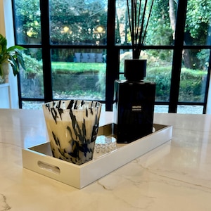 May include: White tray with a black and white patterned candle and a black glass bottle with a gold label that reads "Sences Blanc Almonds".