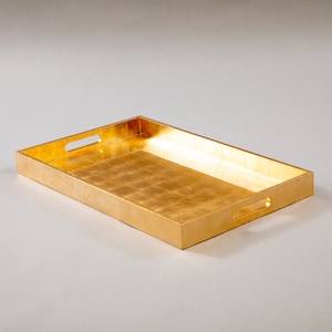 May include: A gold rectangular tray with two handles. The tray is made of wood and has a gold leaf finish.