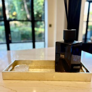May include: A gold tray with a clear glass dish and a black glass bottle with a black cap and black reeds. The bottle has the text "SENSES ALMOND BLOSSOM" on the label.