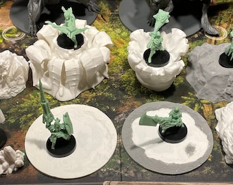 May include: A collection of 3D printed miniature bases for tabletop games. The bases are made of white and gray plastic and feature various designs, including a rocky outcrop, a circular base, and a base with a raised platform. The bases are designed to be used with miniature figures.