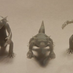 Könnte beinhalten: Fünf kleine, weiße Plastikfiguren von fantastischen Kreaturen. Jede Kreatur hat eine andere Pose und Merkmale, darunter Hörner, Stacheln und Schwänze.