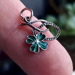 May include: A silver charm with a green four-leaf clover design. The clover is attached to a silver stem with a loop at the top for attaching to a bracelet or necklace.